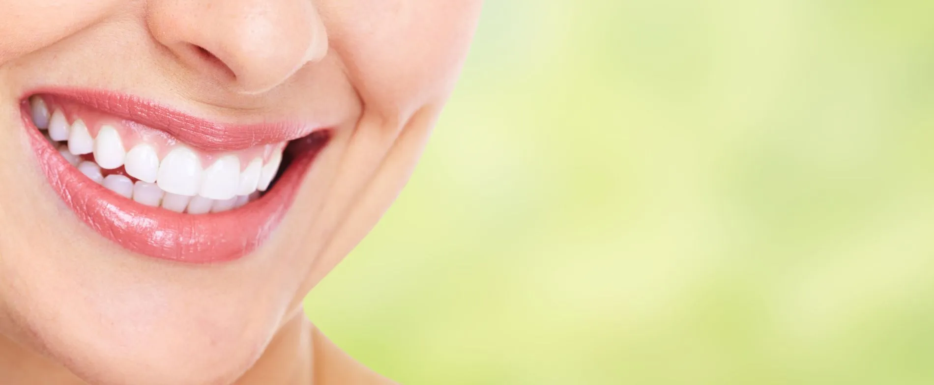 Primo piano di un sorriso femminile con denti bianchi e allineati e labbra rosa lucide su sfondo verde sfocato